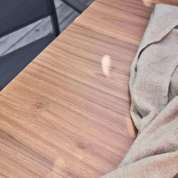 Nahaufnahme einer Tischplatte aus Holz mit sichtbarer Maserung und einem darauf liegenden Leinentuch.