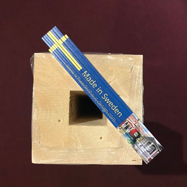 Holzpfosten mit quadratischer Hohlöffnung und ein darauf liegender, zusammengeklappter Zollstock.