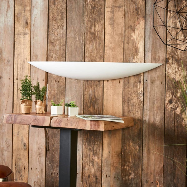 Moderne gebogene weiße Wandleuchte an einer rustikalen Holzwand über einem Holztisch mit kleinen Topfpflanzen.