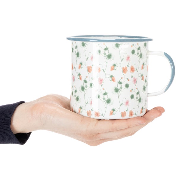 Emaille-Becher mit Blumenmuster, gehalten in einer Hand.