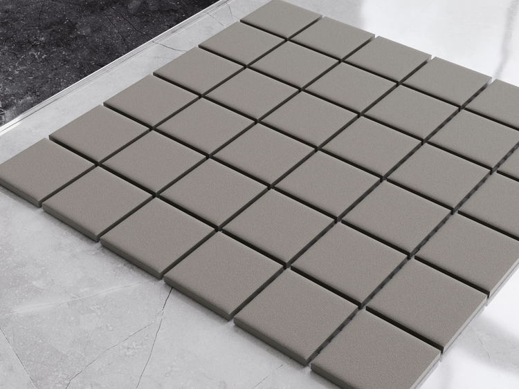 Quadratische Mosaikfliesen mit strukturierter Oberfläche, in einem Gittermuster auf einem Boden ausgelegt.