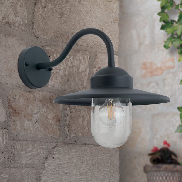 Außenwandleuchte mit gebogenem Arm und klarem Glasdiffusor, montiert an einer Steinwand, mit sichtbarem Filament-Leuchtmittel.