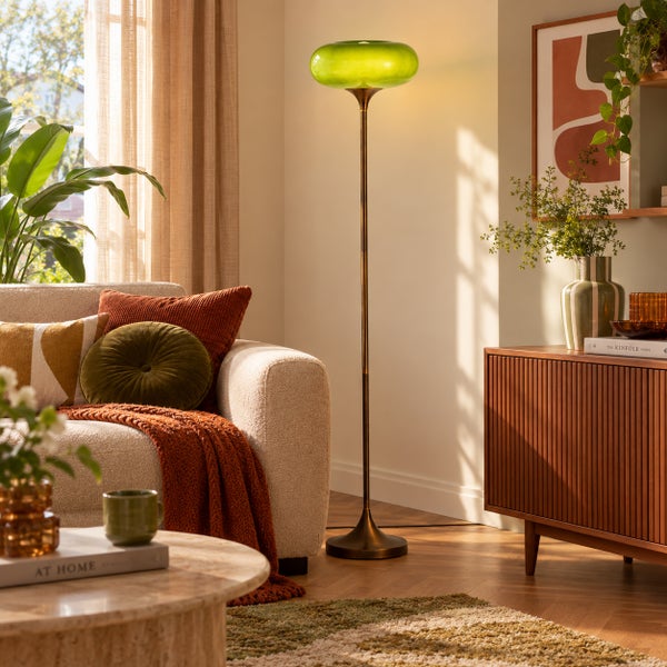 Moderne Stehlampe mit rundem Glas-Lampenschirm und Metall-Standfuß im Wohnzimmer, platziert neben einem Sofa.