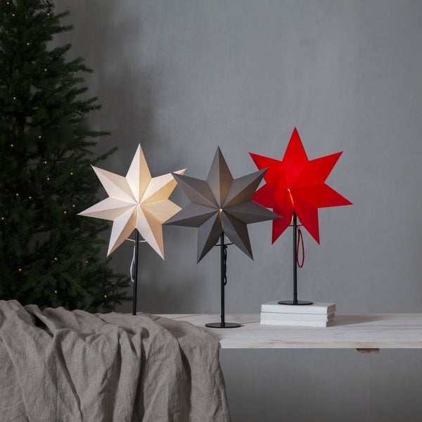 Dekorative Sternleuchten in Gold, Grau und Rot auf einem Tisch neben einem Weihnachtsbaum