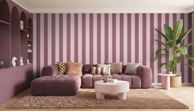 Modernes Wohnzimmer mit gestreifter Tapete in Rosa und Weiß, lila Polstersofa mit Kissen, flauschigem Teppich und runden Couchtischen.