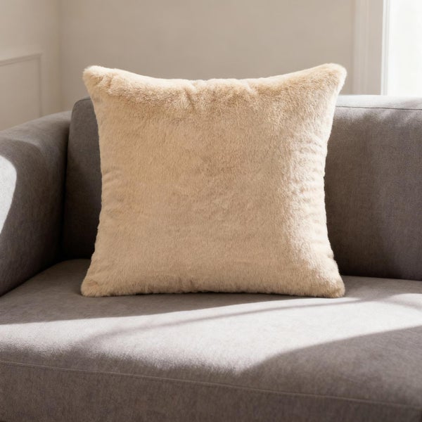 Beige quadratisches Zierkissen aus Kunstfell auf einem grauen Sofa.