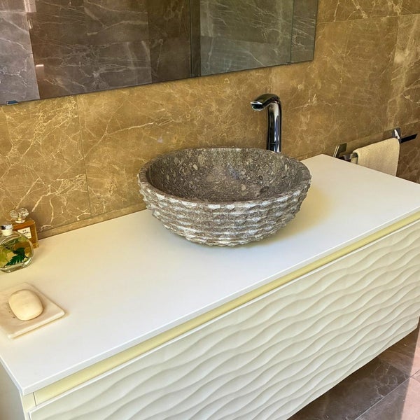 Modernes Badezimmer mit rundem Naturstein-Aufsatzwaschbecken auf weißem Waschtischunterschrank vor Wandfliesen in Marmoroptik.