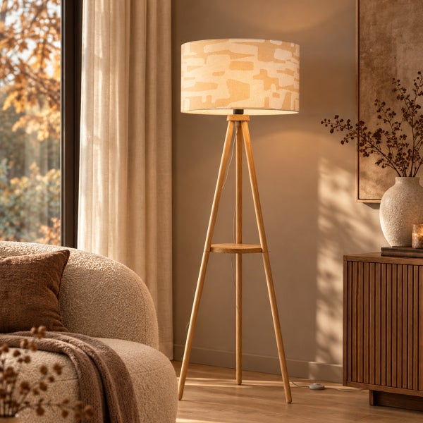 Dreibeinige Stehlampe aus Holz mit gemustertem Lampenschirm in modernem Wohnzimmer mit Sofa und Kommode.