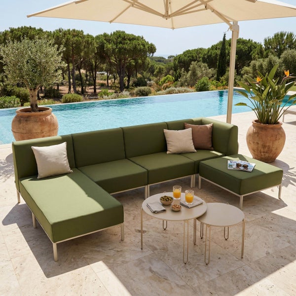Garten-Lounge-Set mit grünem Ecksofa, Hocker, zwei runden Beistelltischen und Sonnenschirm auf einer Terrasse am Pool.
