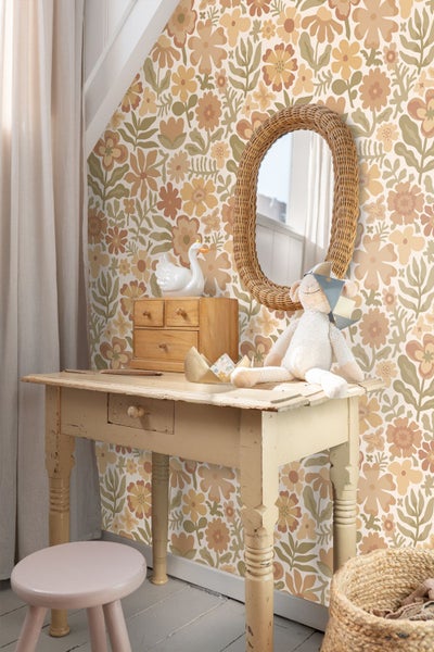 Retro-Kinderzimmer mit floraler Tapete in warmen Farbtönen, antikem Holztisch, Stofftier und einem ovalen Spiegel mit Rahmen aus Rattan.