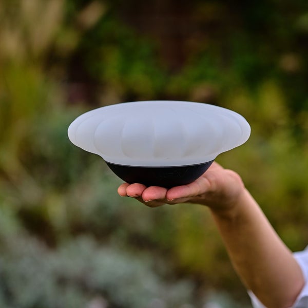Eine Person hält eine runde Aussenleuchte mit einem Lampenschirm in der Hand.