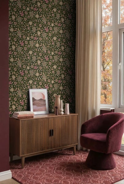 Vliestapete mit floralem Muster in Grün, Rosa und Beige an einer Wand hinter einer hölzernen Kommode und einem Sessel in einem hellen Zimmer.