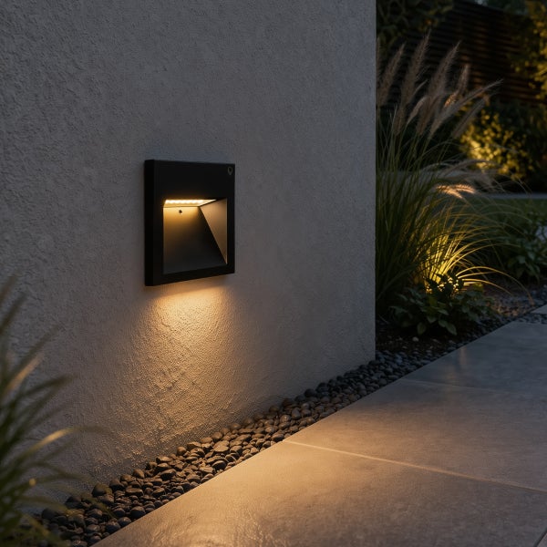 Schwarze LED Außenwandleuchte an einer verputzten Wand beleuchtet einen Gehweg mit Kies und Steinplatten.