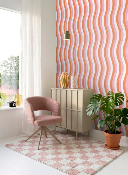 Helles Zimmer mit Wellen-Retro-Tapete, einem rosa Sessel, einem beigen Sideboard, einem karierten Teppich und einer Monstera-Pflanze.