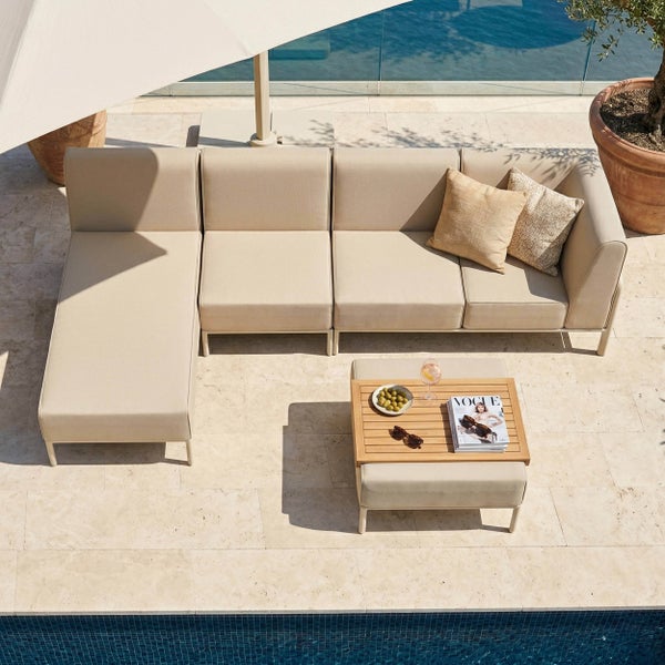 Modulares Garten-Lounge-Set aus beigefarbenem Stoff mit passendem Hockertisch auf einer hellen Steinterrasse am Pool.