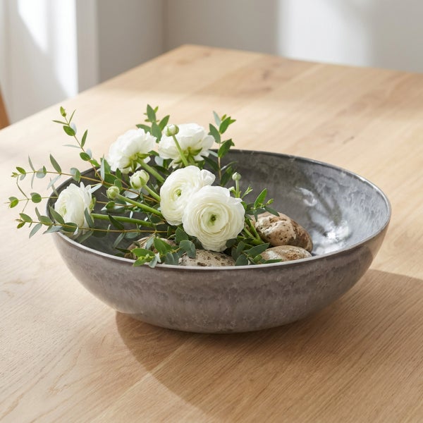Dekorative Schale aus Keramik mit weißem Blumenstrauß und Steinen auf einem Holztisch.
