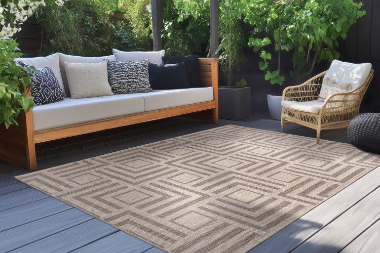 Outdoor Teppich mit geometrischem Muster auf einer Terrasse mit Holzsofa und Korbsessel.
