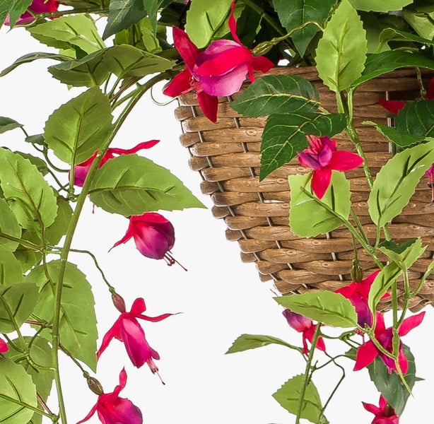 Künstliche Hänge-Fuchsie in einem geflochtenen Weidenkorb mit grünen Blättern und rosa Blüten.