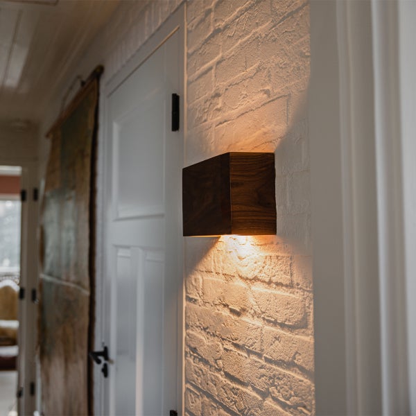 Moderne Wandleuchte aus Holz in Quaderform montiert an einer weissen Backsteinwand in einem Wohnbereich.
