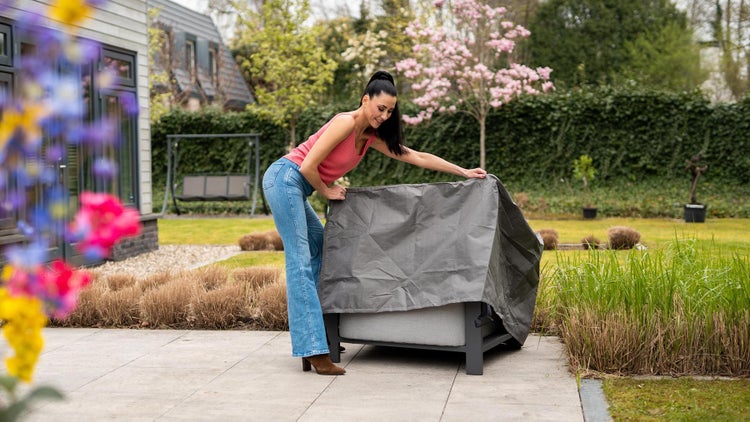 Frau deckt Gartenmöbel mit einer Schutzhülle ab.