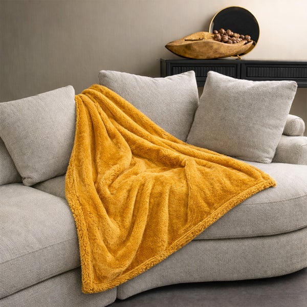Eine weiche Wohndecke auf einem modernen Polstersofa mit Zierkissen und Dekoration im Wohnzimmer.