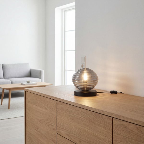 Moderne Tischleuchte mit geriffeltem Glaskolben auf einem Holz-Sideboard in einem hellen, aufgeräumten Wohnzimmer mit Sofa und Couchtisch.