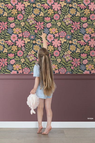 Ein Kind steht vor einer Wand mit floraler Tapete und dunkelvioletter Wandtäfelung auf einem hellen Holzboden.