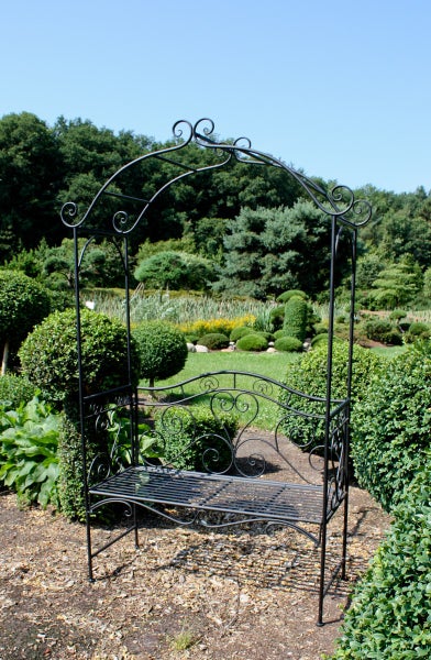 Schwarze Gartenbank aus Metall mit integriertem Rosenbogen und dekorativen Verzierungen in einer Gartenanlage.