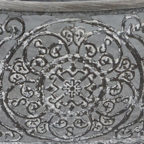 Detail eines verzierten Metallmusters an einem Gartenmöbel mit antiker Optik und floralem Ornament.