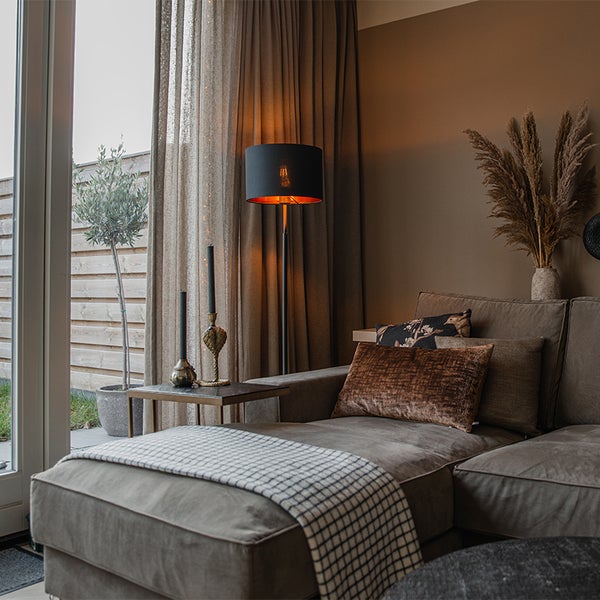 Warm beleuchtetes Wohnzimmer mit Stoffsofa, Metall-Stehleuchte, Beistelltisch und Vorhängen im modernen Stil mit Naturmaterialien.