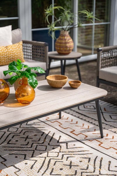 Moderne Terrasse mit Gartenmöbeln: Lounge-Sofa, Couchtisch in Holzoptik auf einem gemusterten Teppich, dekoriert mit Glasvasen und Holzschalen.