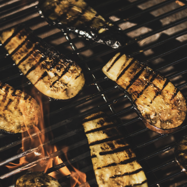 Gegrillte Auberginenscheiben auf einem Grillrost über offener Flamme.