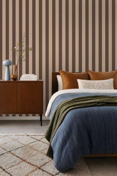 Modernes Schlafzimmer mit gestreifter Tapete, einem Holzsideboard, einem Bett mit blauer Tagesdecke und einem gemusterten Teppich.