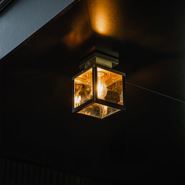 Industrielle quadratische Deckenleuchte mit schwarzem Metallrahmen und klaren Glasscheiben, die warmes Licht ausstrahlt.