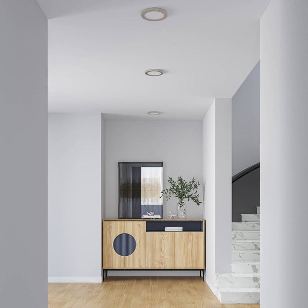 Hell gestalteter Flur mit drei runden Einbaustrahlern an der Decke über einem Sideboard aus Holz.