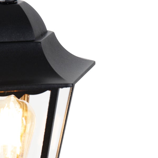 Nahaufnahme einer schwarzen Außenwandleuchte im Laternen-Stil mit Glaseinsätzen und leuchtendem LED-Filament-Leuchtmittel.