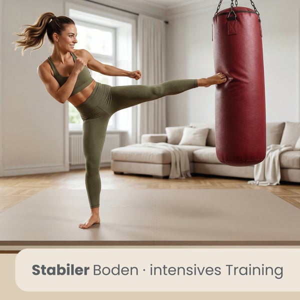 Frau tritt auf einer hellbraunen Bodenschutzmatte gegen einen Boxsack in einem hellen Wohnzimmer. Text Stabiler Boden intensives Training.