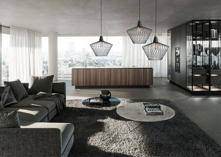 Heller Wohn- und Kochbereich mit drei schwarzen Pendelleuchten im Käfig-Design über einer hölzernen Kücheninsel, grauem Sofa und Couchtischen.