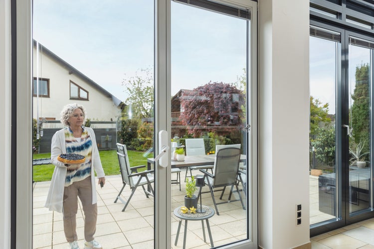 Große Terrassentüren aus Glas bieten einen Blick auf eine helle Terrasse mit Gartenmöbeln und schaffen einen fließenden Übergang nach draußen.