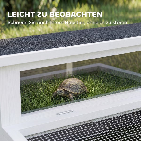 Weißes Schildkrötenhaus aus Holz mit großem Sichtfenster und dunklem Dach, eine Schildkröte befindet sich im Inneren auf Gras.
