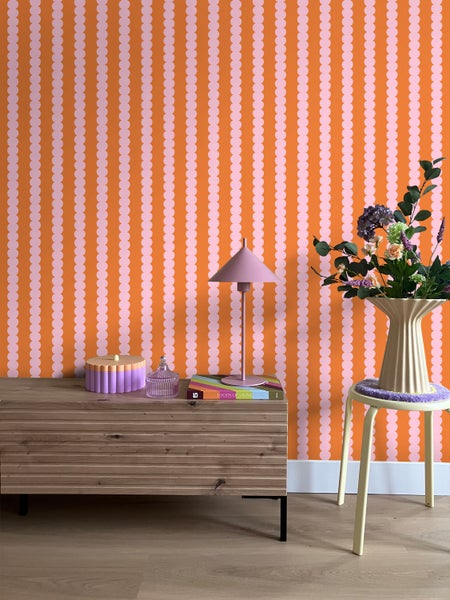 Szene mit Holzkommode, Lampe und Blumen vor einer Wand mit gepunkteter Tapete