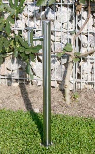 Gartenwasserzapfstelle aus Edelstahl mit einem Wasserhahn, installiert auf einer Rasenfläche vor einer Gabionenwand.