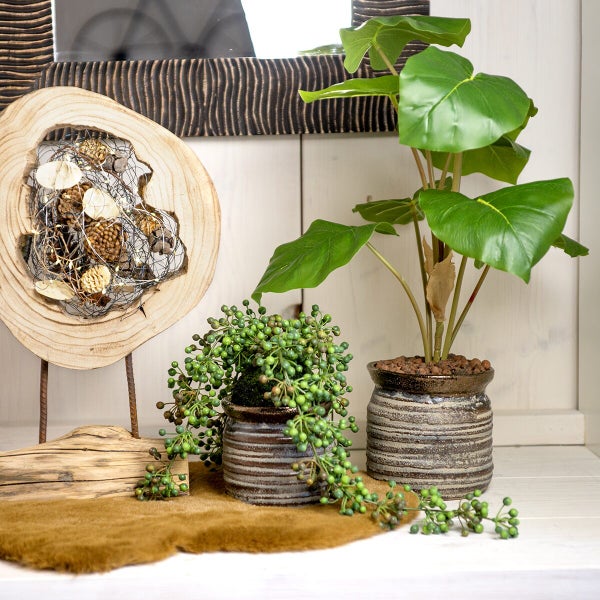 Dekorative Szene mit Kunstpflanzen, hängenden Beeren und einer Holzskulptur mit Naturmaterialien auf einem Regal.