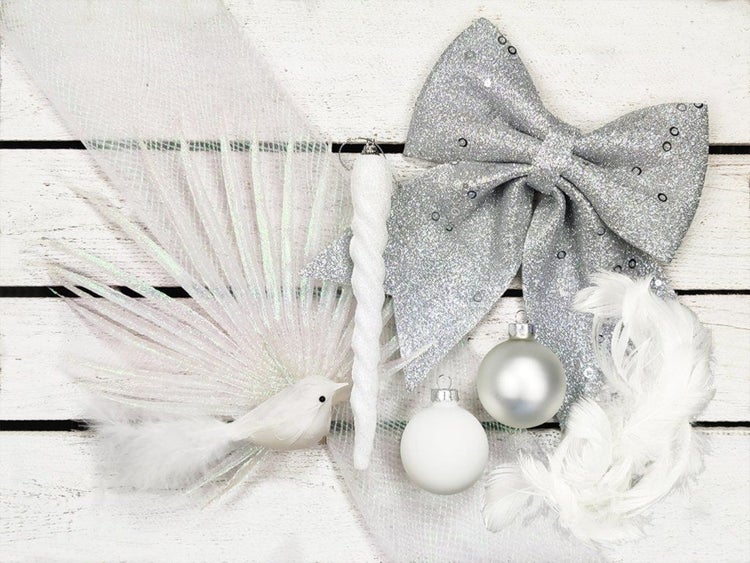 Weihnachtsdekoration Set mit glitzernder Schleife, zwei Weihnachtskugeln, Eiszapfen-Anhänger und Vogel-Figur auf weißem Holzuntergrund.