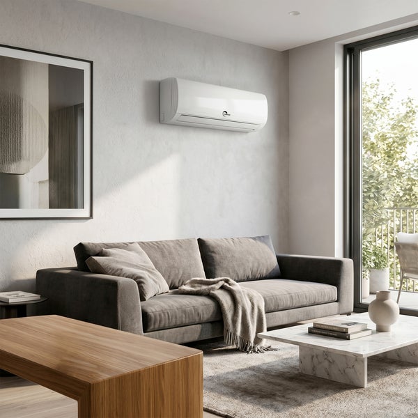 Weißes Wandklimagerät in einem hellen, modern eingerichteten Wohnzimmer mit grauem Sofa, Couchtisch aus Marmor und großen Fenstern.