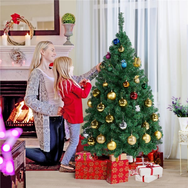 Mutter und Tochter schmücken einen Weihnachtsbaum im Wohnzimmer mit Christbaumkugeln, umgeben von Geschenken.