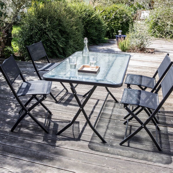 Gartenmöbel-Set bestehend aus einem rechteckigen Tisch mit Glasplatte und vier Klappstühlen mit Netzbespannung auf einer Holzterrasse.