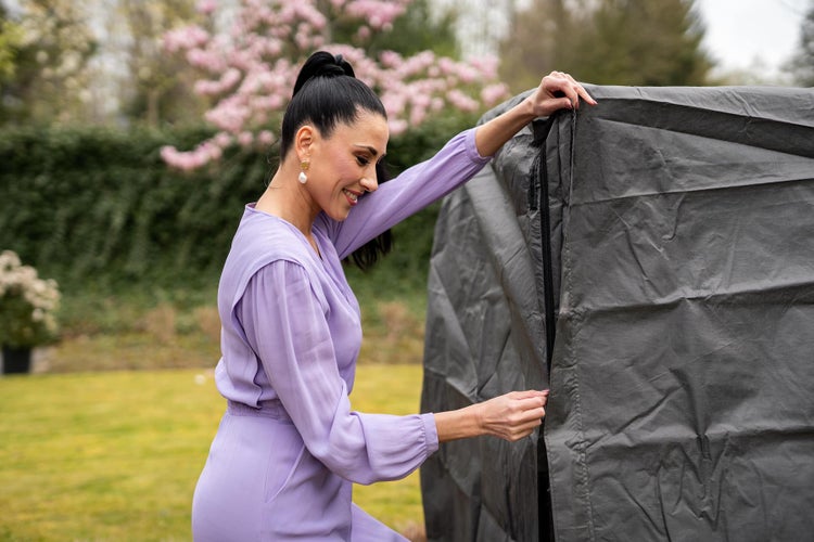 Eine Frau öffnet eine graue Schutzhülle im Garten.