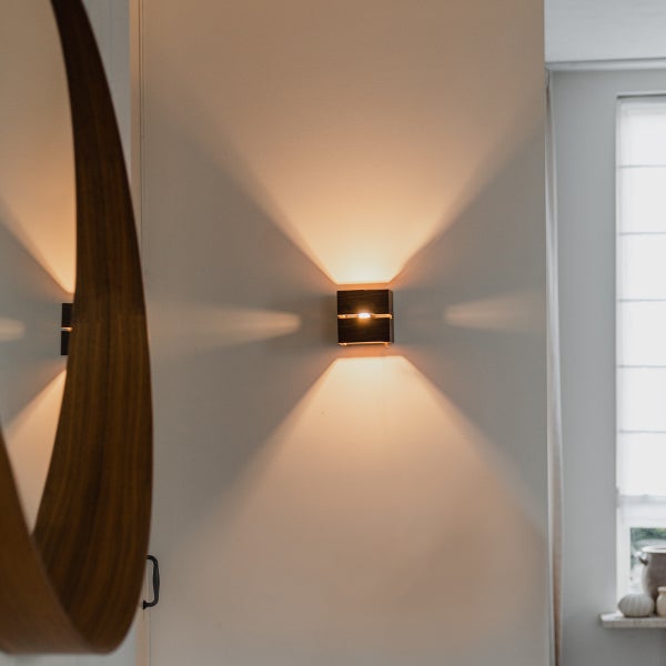 Moderne quadratische Wandleuchte aus Holz mit indirektem Lichtkegel nach oben und unten in einem eleganten Wohnbereich