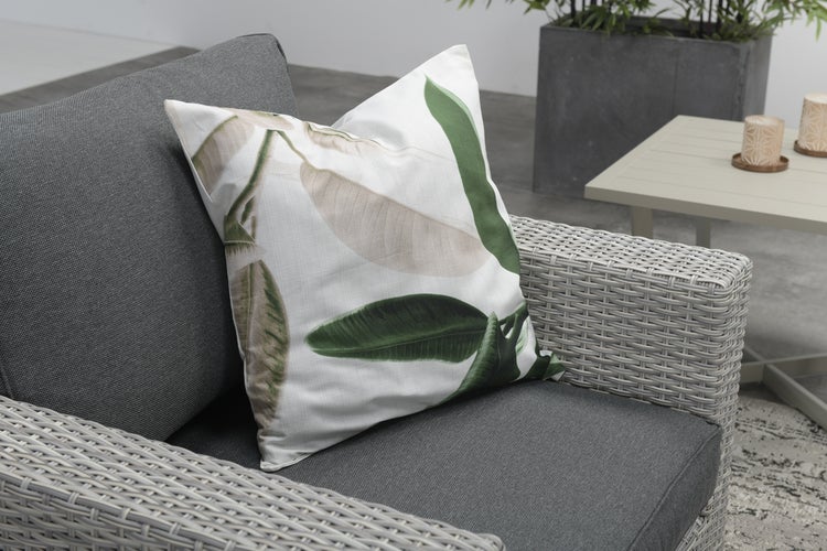 Quadratisches Dekokissen mit botanischem Blattmuster auf einem grauen Gartenstuhl aus Polyrattan.
